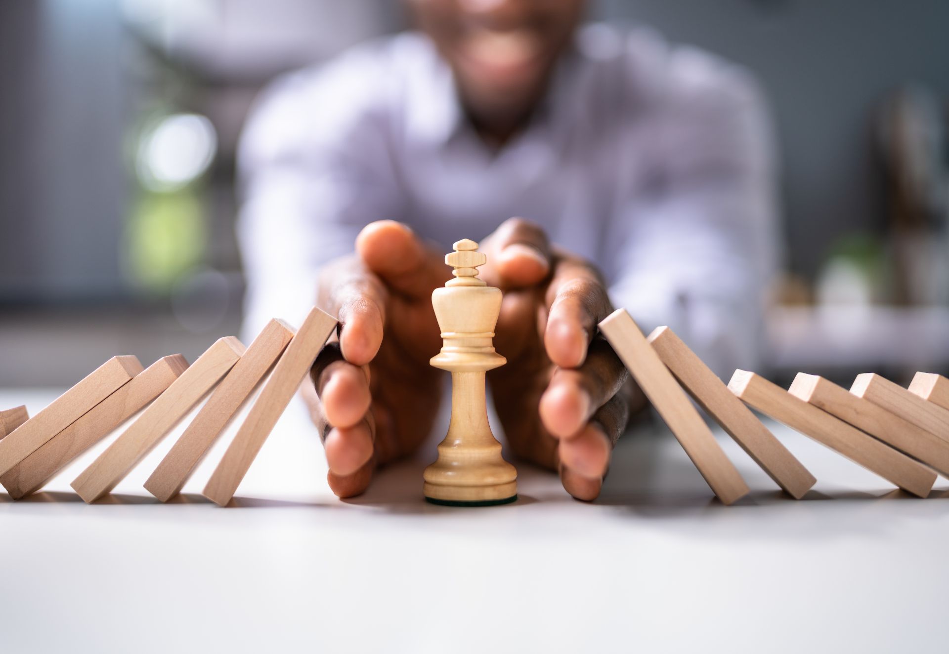 a man protecting a chess piece from falling dominos